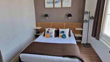Habitación de hotel ordenada con cama, mesitas de noche, lámpara y decoración en la pared.