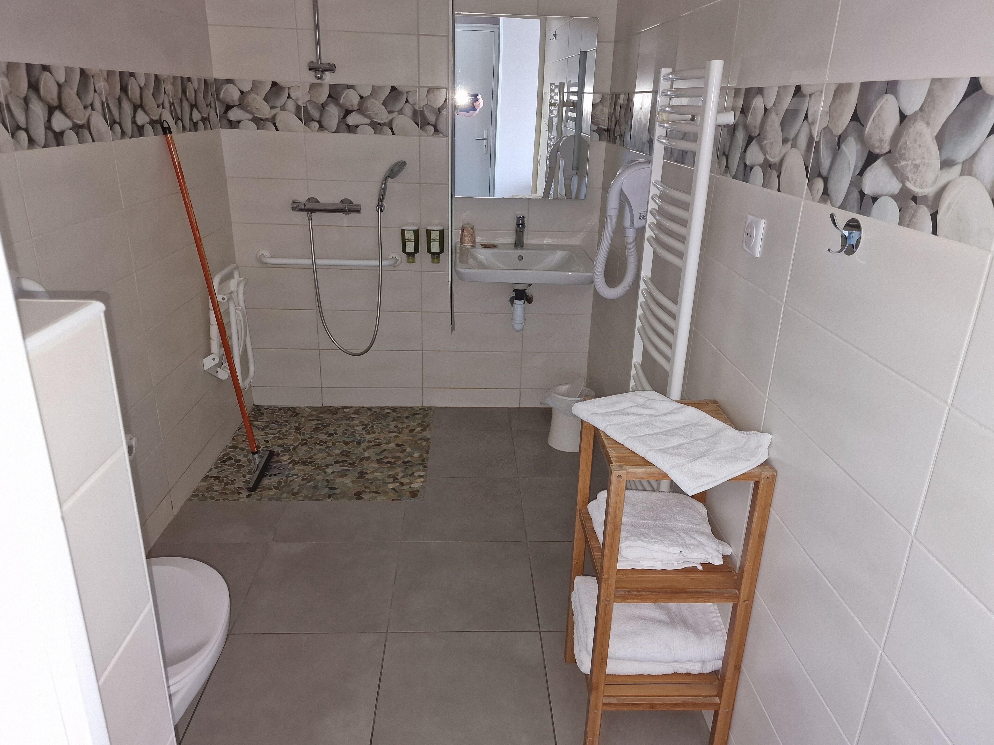 A bathroom with a toilet, sink, shower, and a wooden shelf with towels.