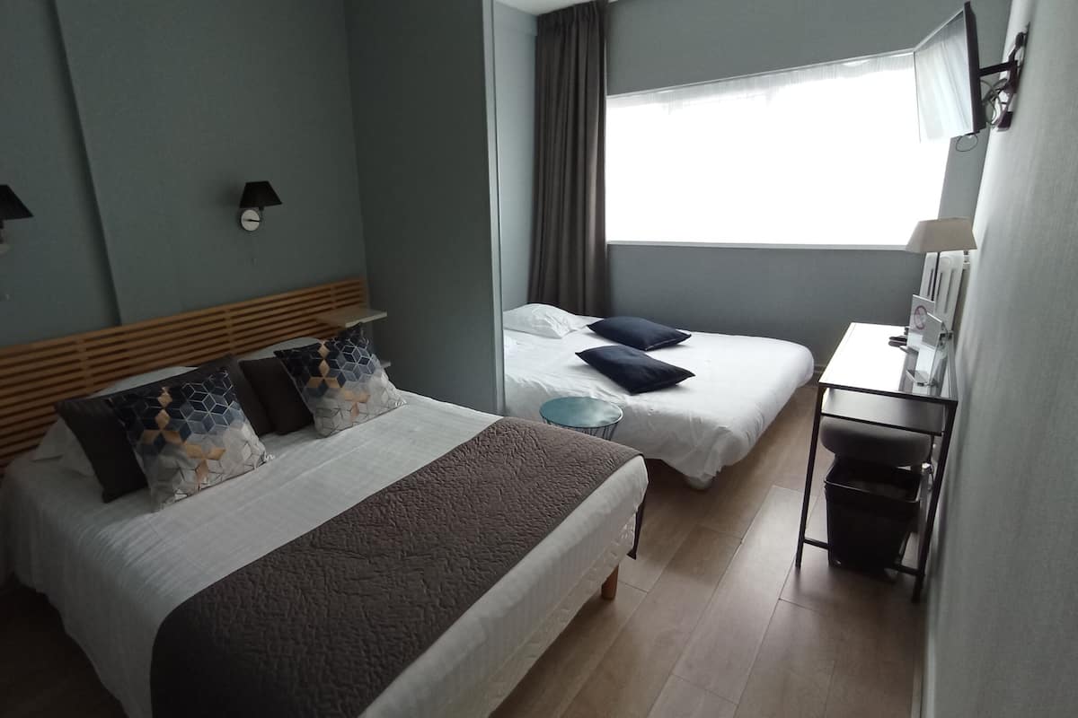 Une chambre d’hôtel avec un grand lit, un lit plus petit, un bureau et une fenêtre avec des rideaux.