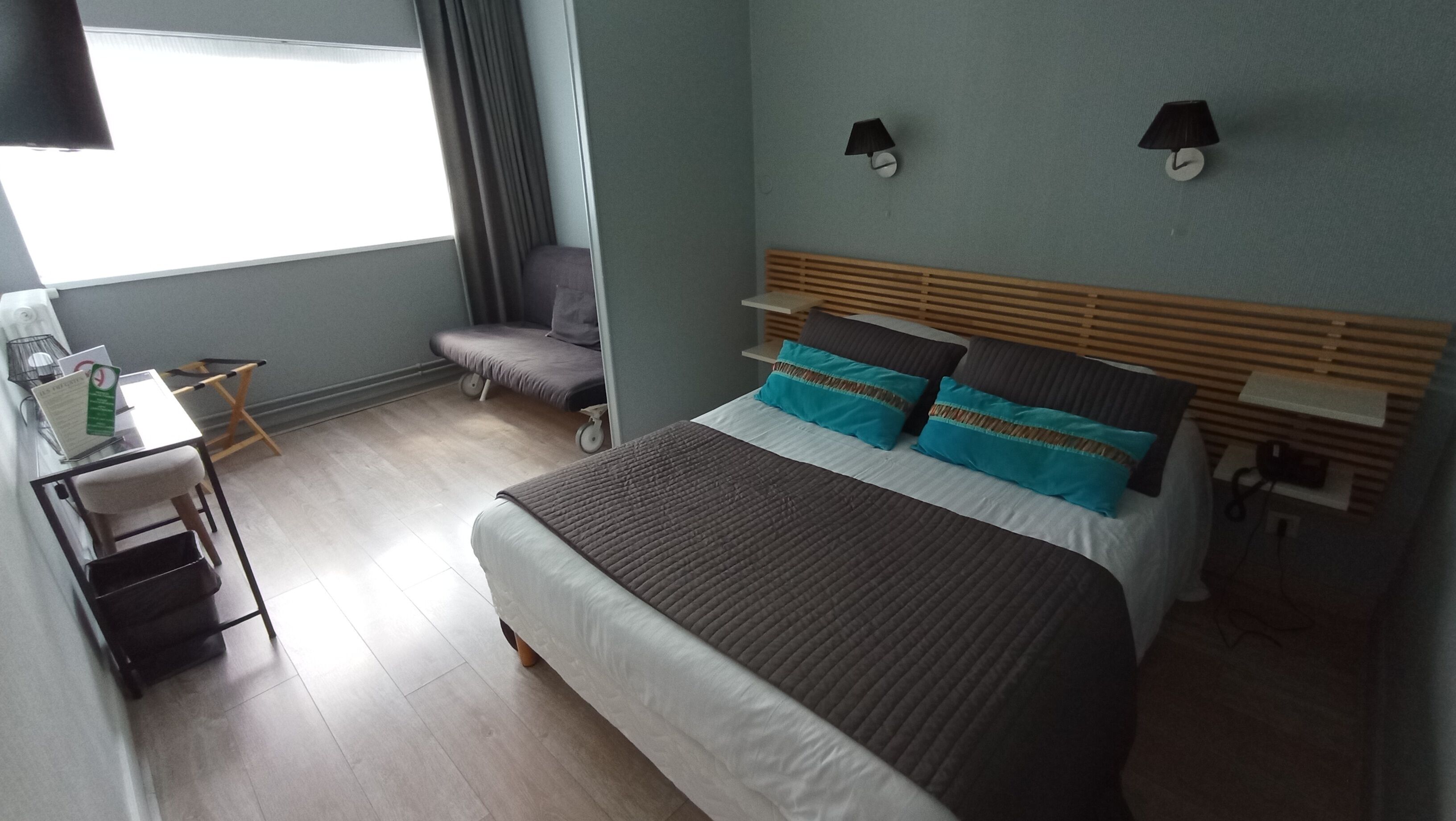 Una habitación de hotel con cama, mesitas de noche, escritorio, silla y ventana con cortinas.