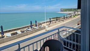 A seaside view from a balcony overlooking a beach with sun loungers and umbrellas, a promenade, and a cliff in the distance. - Les Fregates (Veulettes-sur-Mer)
