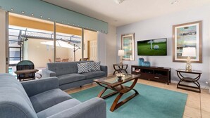 A living room with a sofa, a coffee table, a TV, and a grill outside the window.
