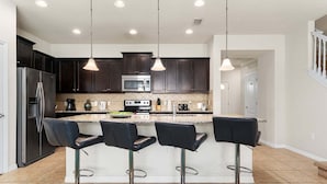 A modern kitchen with dark cabinets, stainless steel appliances, and a central island with bar stools.