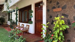 A stone wall with a sign reading "Sharon Inn," a wooden door, and outdoor seating with chairs and tables. - Sharon Inn (Kandy)