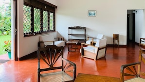 A spacious room with a wooden floor, a large window with a lattice design, and a seating area with two sofas and two chairs. - Sharon Inn (Kandy)