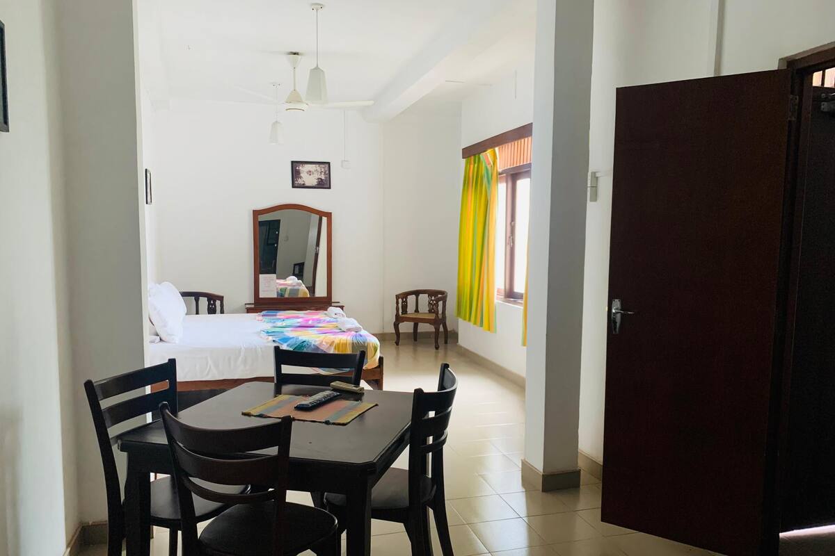 Habitación de hotel con cama, escritorio y silla. Hay una ventana con cortinas, una puerta y un espejo en la pared.