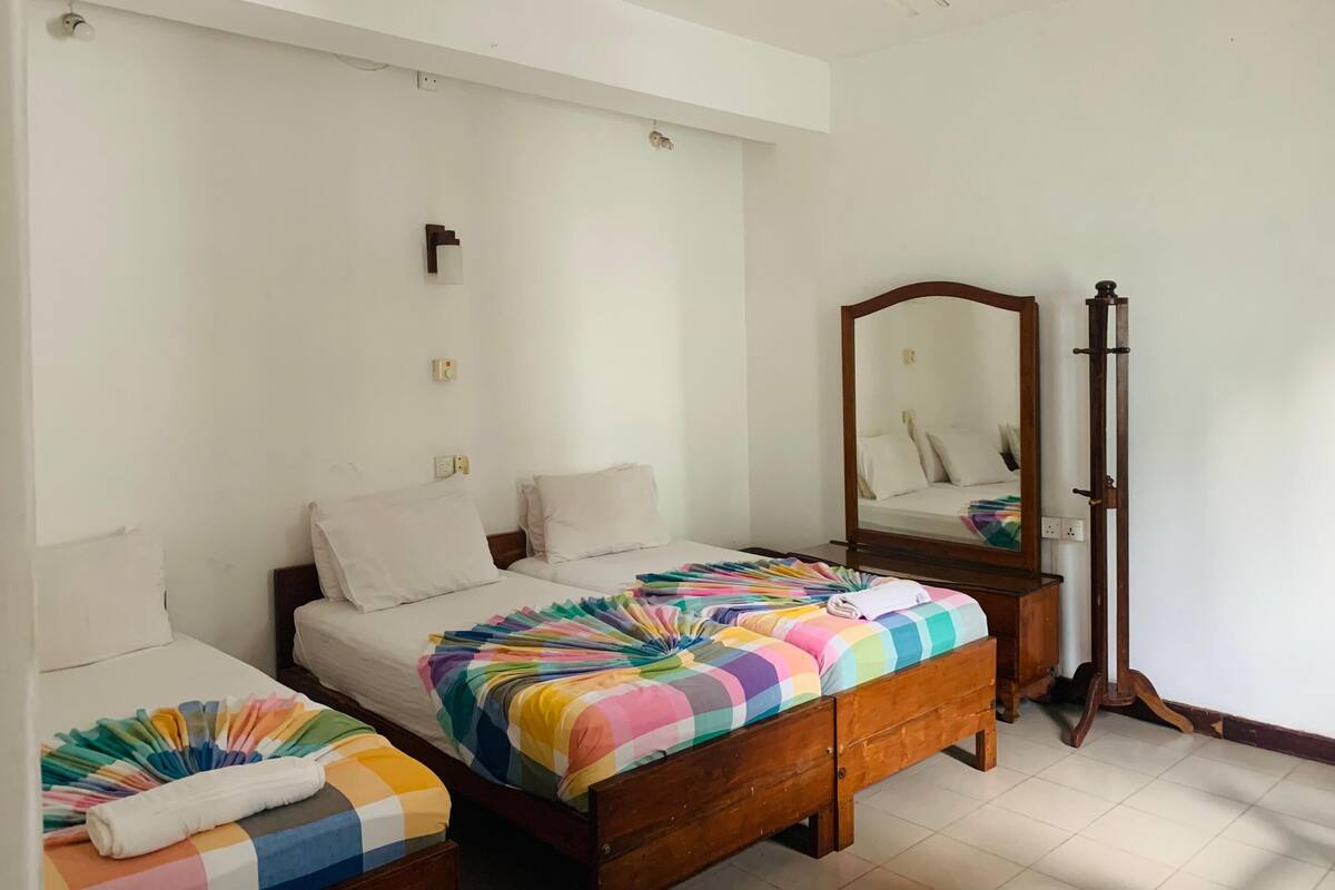 Un dormitorio con dos camas, un armario de madera, un espejo y un ventilador de techo.