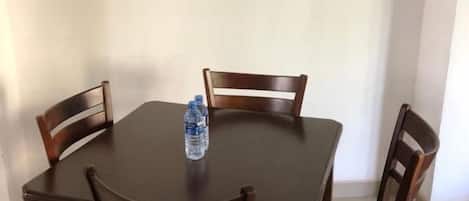 Una mesa de comedor con cuatro sillas de madera, una botella de agua sobre la mesa y un cuadro enmarcado en la pared.