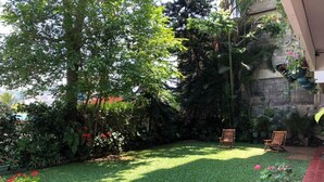 A well-maintained garden with a lawn, two wooden chairs, and various potted plants. - Sharon Inn (Kandy)