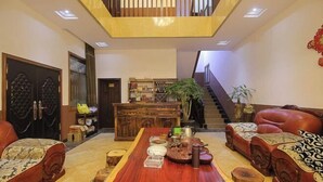 A spacious living area with a wooden coffee table, leather sofas, a staircase, and a bookshelf. - Shizong Donglai Inn (Shizong)