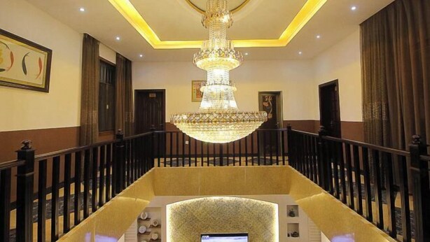 A grand staircase with a chandelier, a wall-mounted television, and a patterned wall at the bottom. - Shizong Donglai Inn (Shizong)