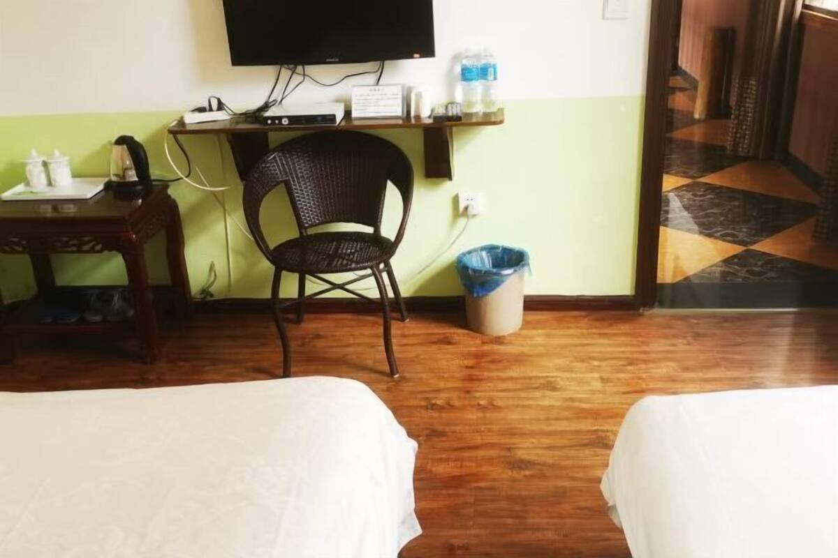 A hotel room with two beds, a desk with a chair, a television, and a trash bin.