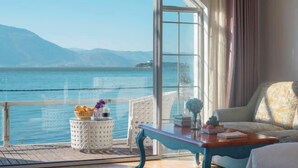 A room with a large window overlooking a body of water and mountains. There is a white wicker side table with a basket and a vase. A blue table with a book and a vase is in the foreground. - Erhai Lake View Resort Hotel Yuebo Jingyi (Dali City)
