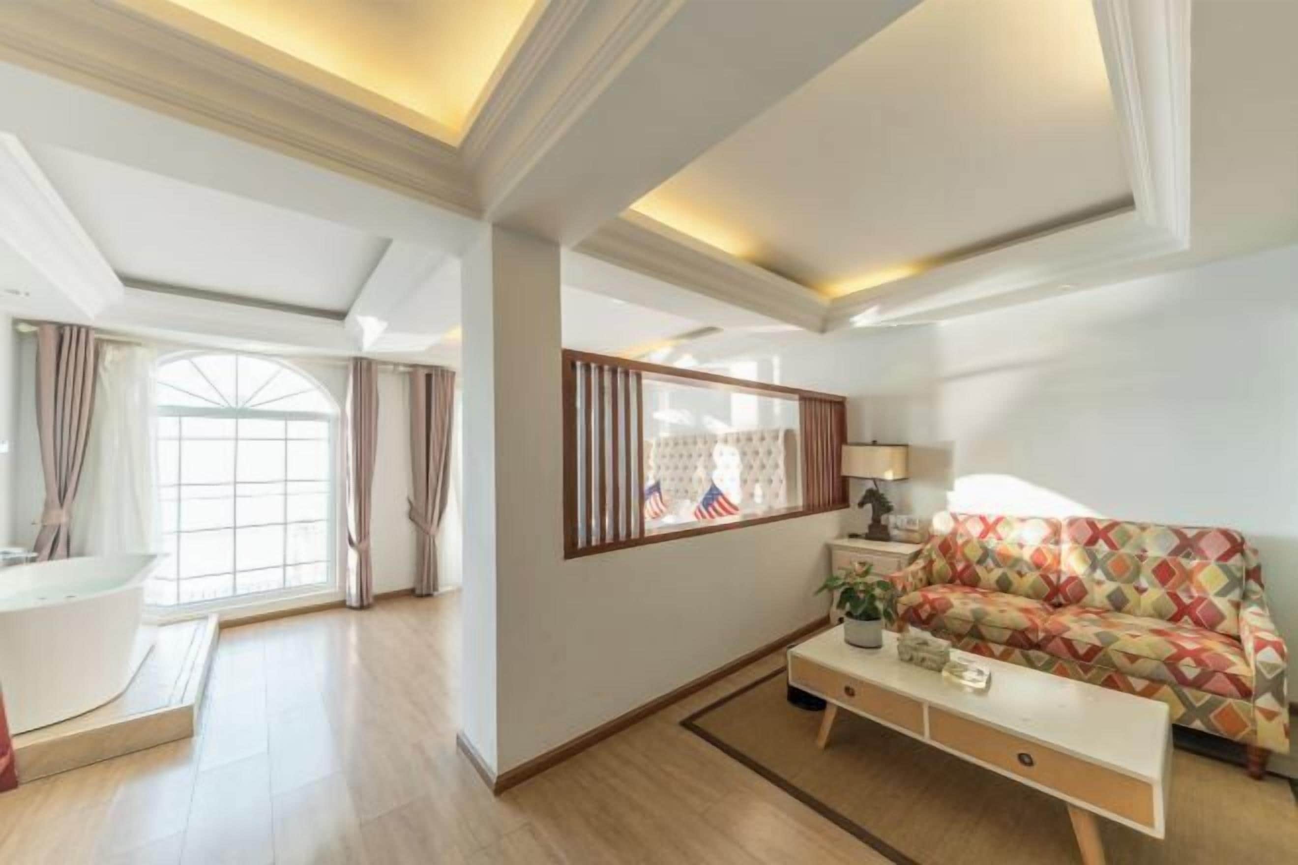 A spacious living room with a large window, a sofa, a coffee table, and a side table with a lamp.