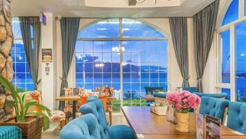 A hotel room with a large arched window, a seating area with blue sofas, and a dining table.