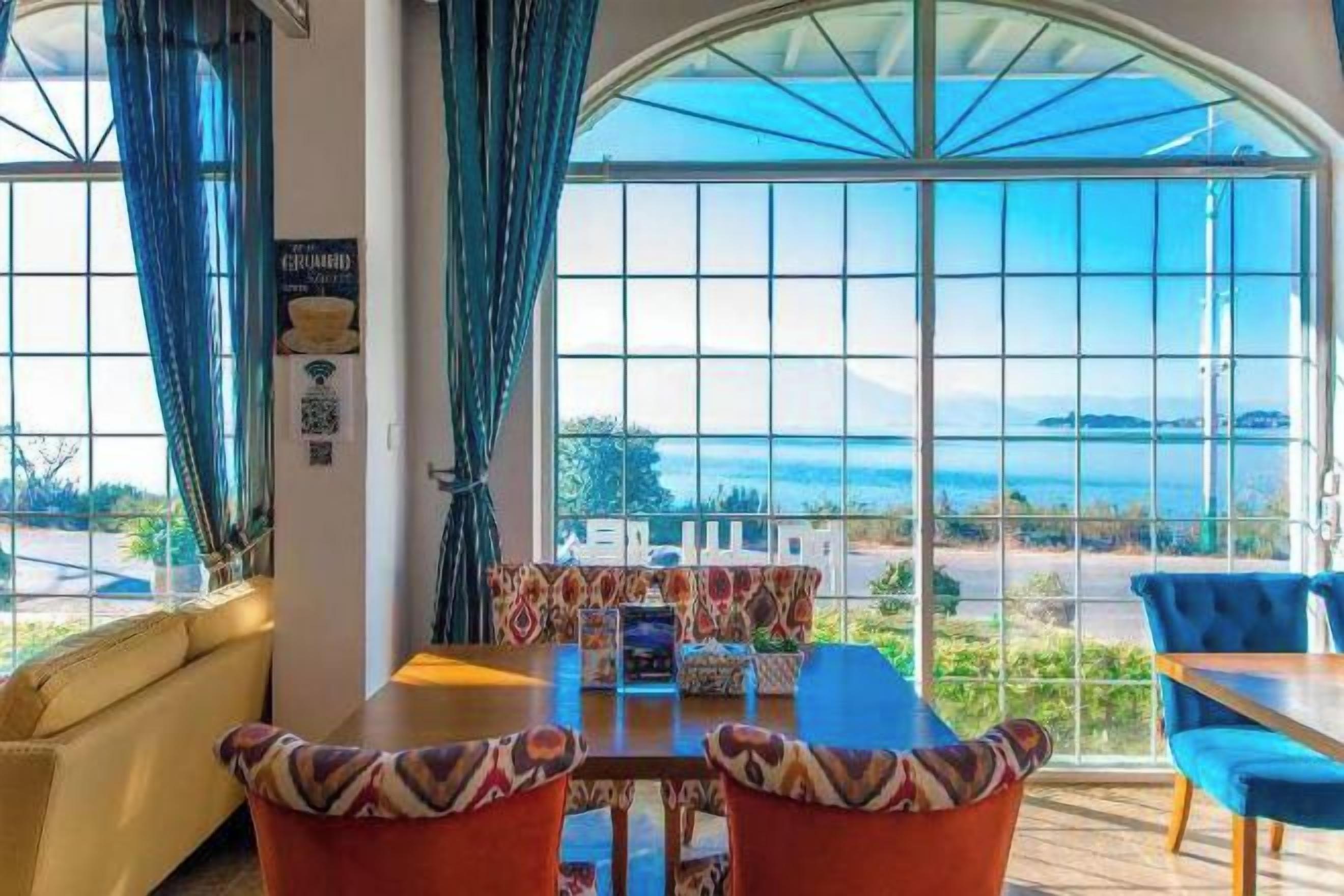 Un comedor con mesa y sillas, ventanas amplias con vista al mar y un sofá.