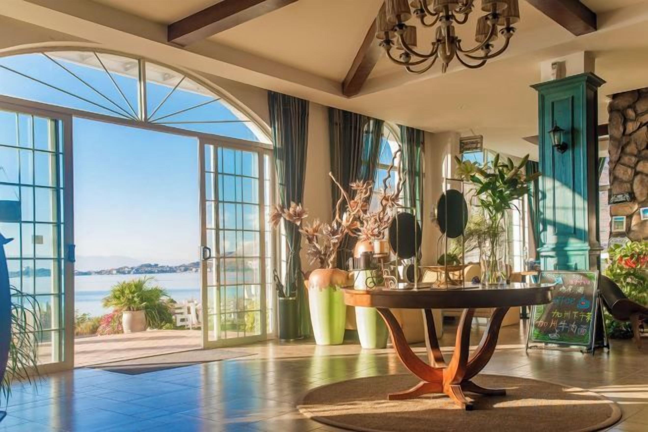 Una habitación amplia con un gran ventanal que da a una vista panorámica, una mesa redonda con un jarrón de flores y un mueble de color turquesa.