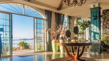 Una habitación amplia con un gran ventanal que da a una vista panorámica, una mesa redonda con un jarrón de flores y un mueble de color turquesa.