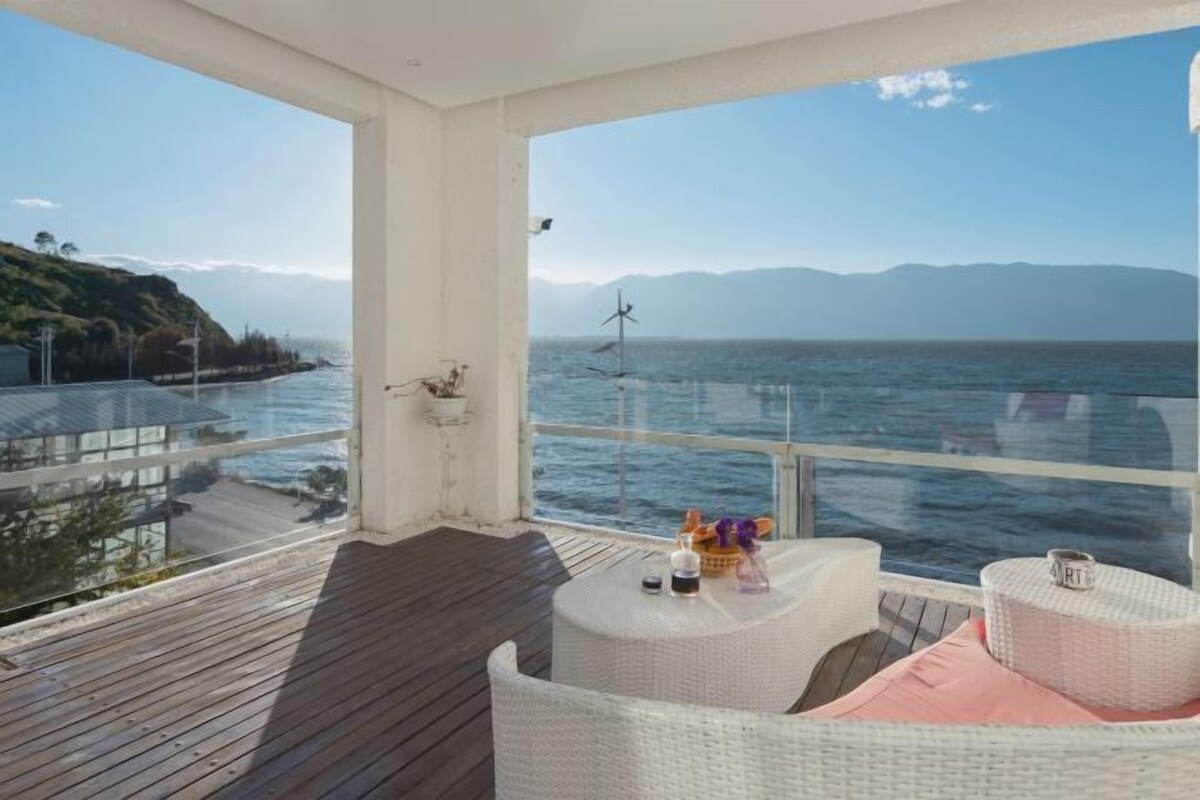 Un balcón con vistas al mar, una turbina eólica y una mesa con objetos encima.