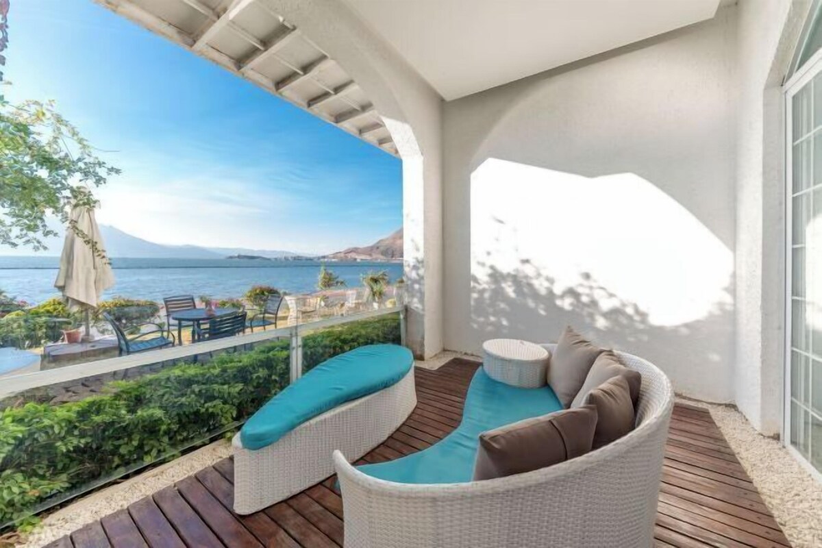 Un balcón con mobiliario de mimbre, vista al mar y una terraza de madera.