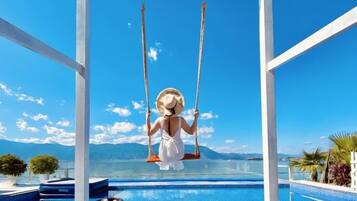A person on a swing over a pool with a clear view of the sky and distant mountains.