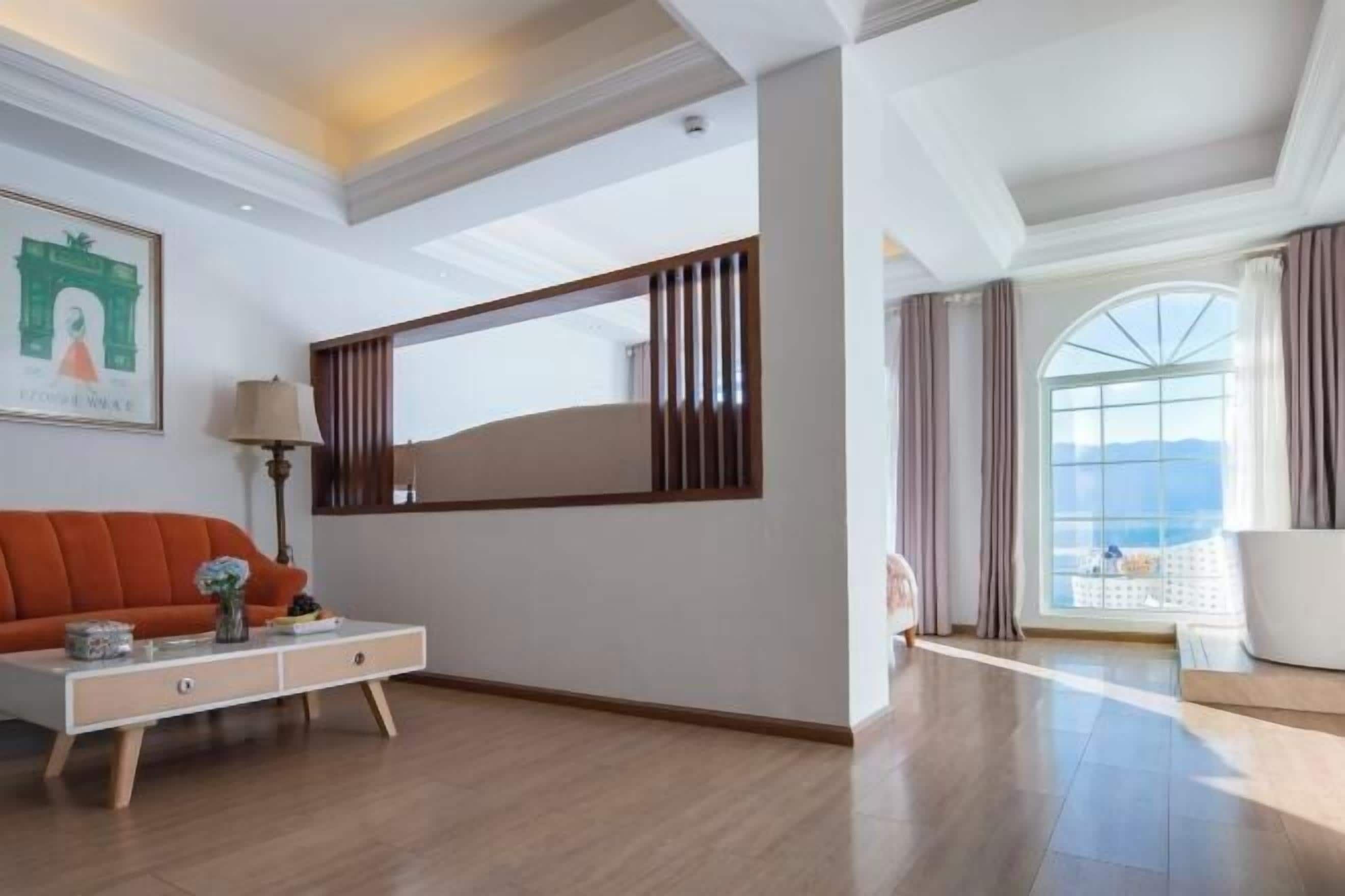 Una habitación de hotel moderna con un ventanal grande, un sofá, una mesita auxiliar y un espejo decorativo.