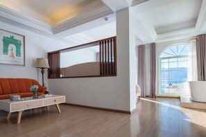 Una habitación de hotel moderna con un ventanal grande, un sofá, una mesita auxiliar y un espejo decorativo.