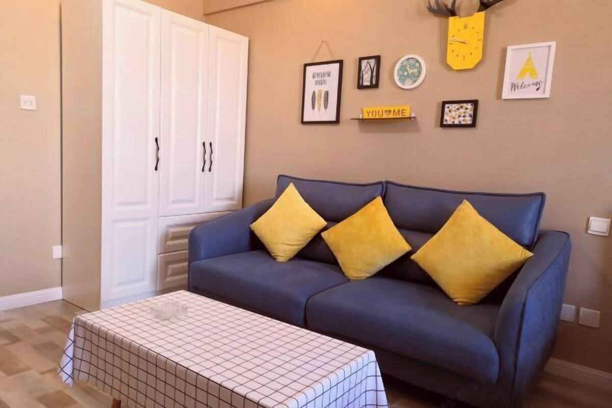 Un salon avec un canapé bleu, trois coussins jaunes, une table basse à motifs et une armoire blanche.