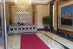 A lobby with a red carpet, a reception desk with a patterned design, a chandelier, a large window with a cityscape view, and a potted plant. - Fashion Express Short-term Rental Apartment (Zhuanghe Xintiandi Huafu Branch) (Zhuanghe)