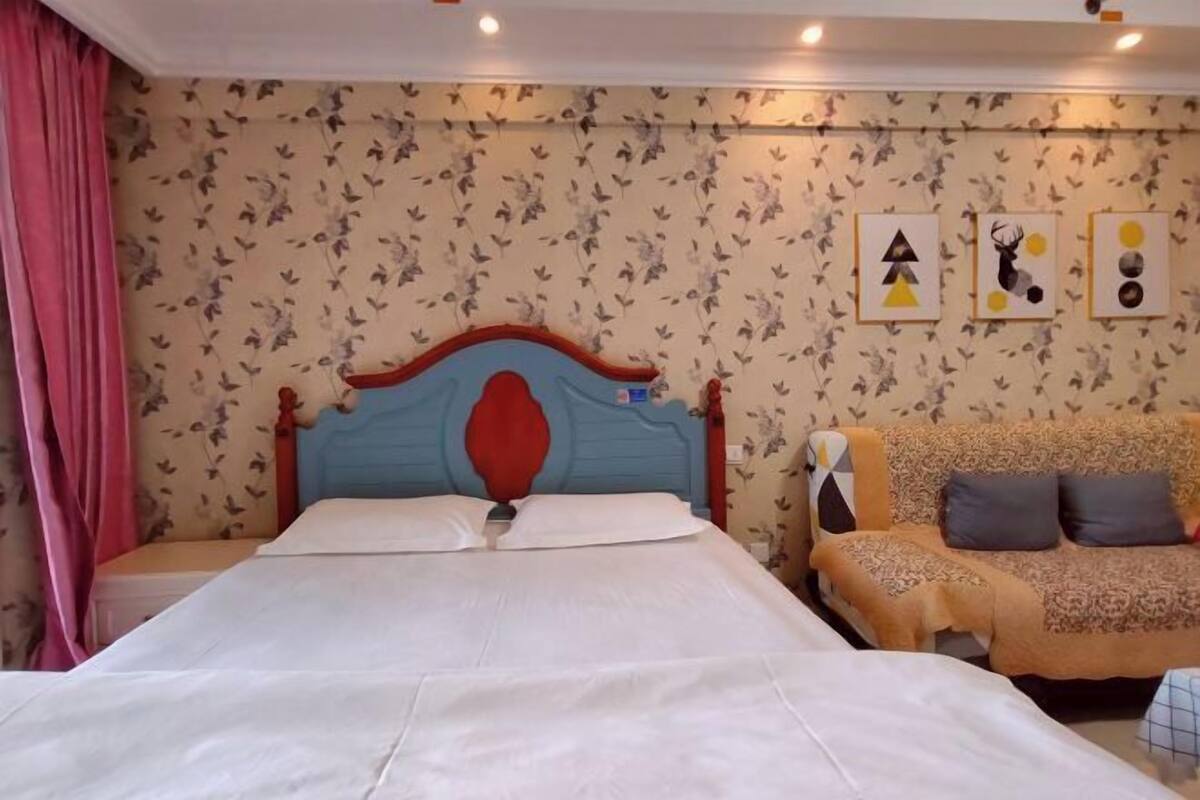 Une chambre à coucher avec un lit, un canapé et un mur recouvert d’un papier peint à motifs floraux et orné d’œuvres d’art abstraites.