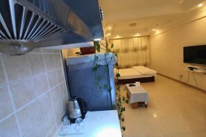 A compact hotel room with a kitchenette, a bed, a TV, and a small table with a checkered tablecloth. - Fashion Express Short-term Rental Apartment (Zhuanghe Xintiandi Huafu Branch) (Zhuanghe)