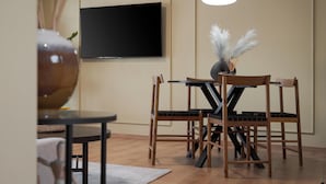 A modern living room with a flat-screen TV mounted on the wall, a round table with chairs, and a decorative vase with feathers. - Aria Luxury Apartment (Patras)