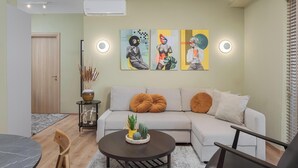 A modern living room with a grey sofa, a coffee table with a plant, and a dining area with a wooden chair. - Aria Luxury Apartment (Patras)