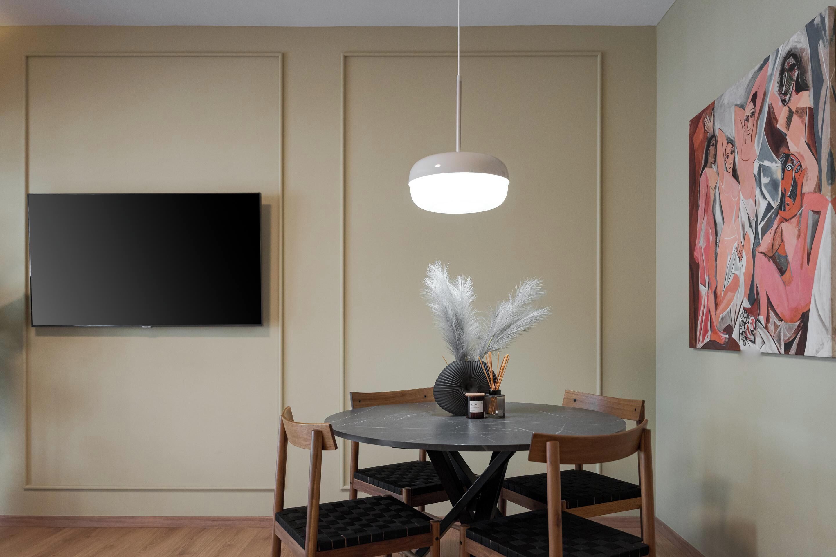 Un coin repas comprenant une table ronde, des chaises, un téléviseur à écran plat et un luminaire suspendu au design moderne.