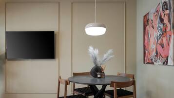 Un coin repas comprenant une table ronde, des chaises, un téléviseur à écran plat et un luminaire suspendu au design moderne.