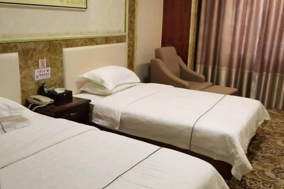 A hotel room with two beds, a chair, a bedside table with a phone, and a curtain.