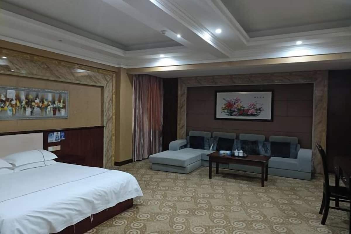 A hotel room with a bed, a sofa, a small table, and a wall-mounted TV.