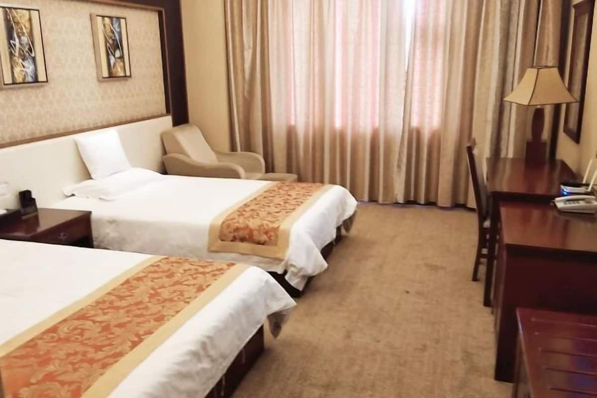 A hotel room with two beds, a desk, a chair, and a lamp.