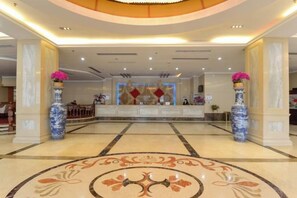 A hotel lobby with a reception desk, two large vases with flowers, and a patterned floor. - Xianju Western International Hotel (Xianju)