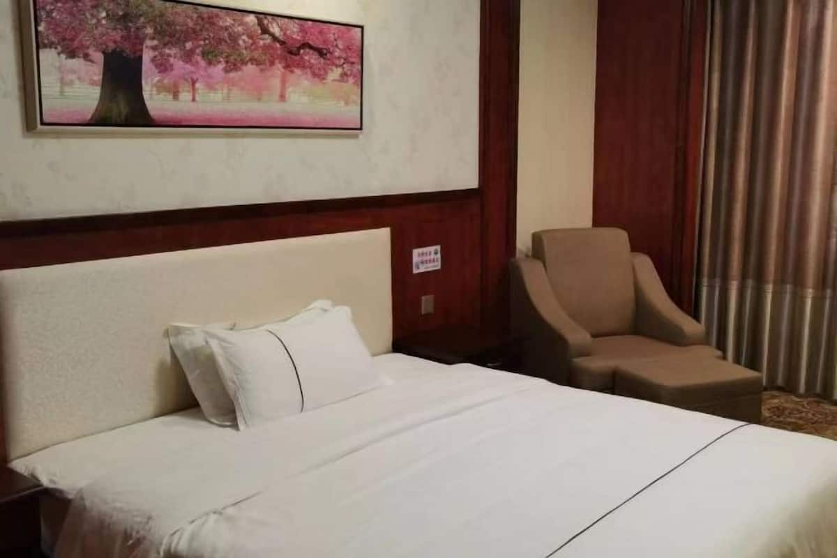 A hotel room with a bed, a chair, and a painting of cherry blossoms on the wall.