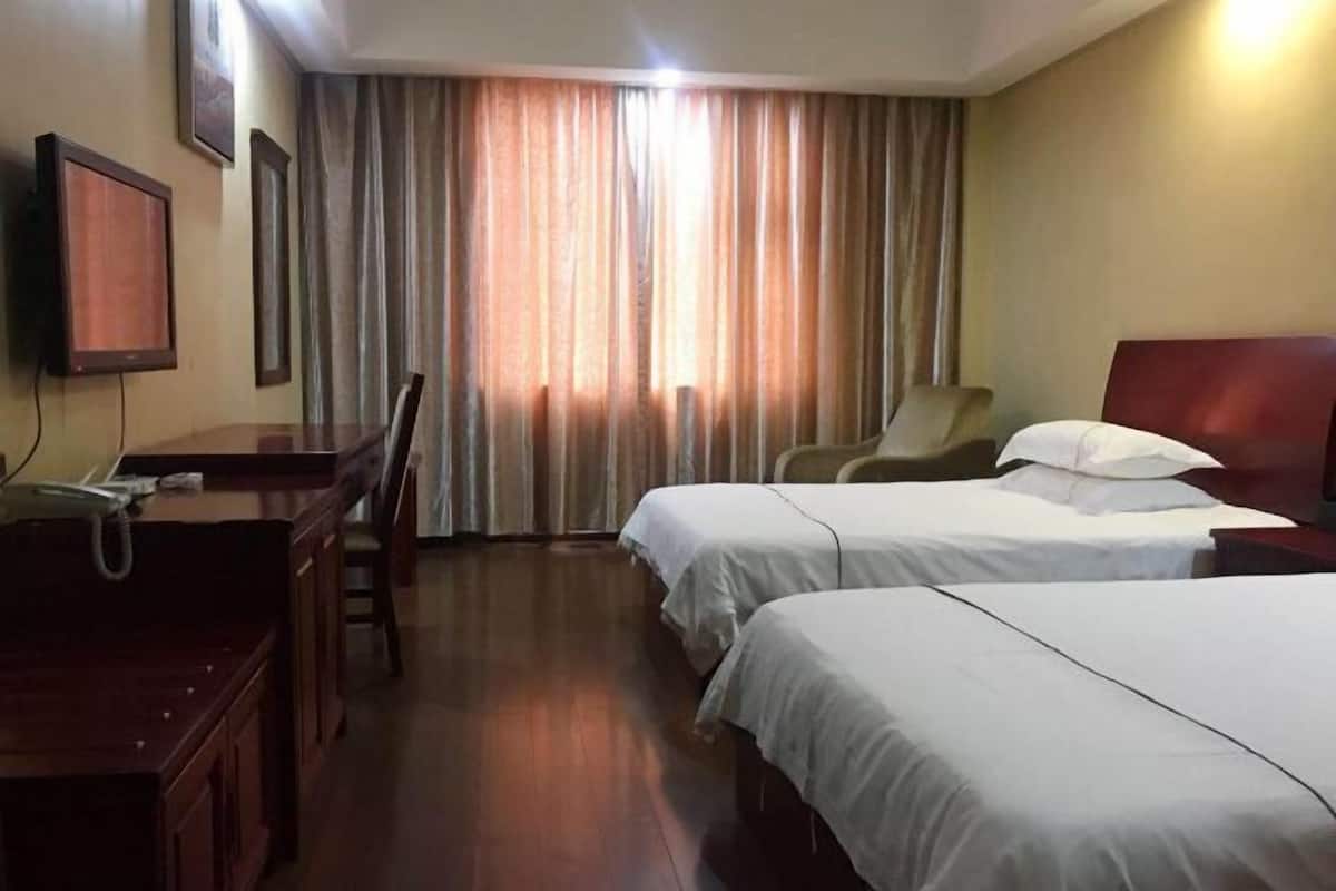 A hotel room with two beds, a desk, a chair, and a TV.