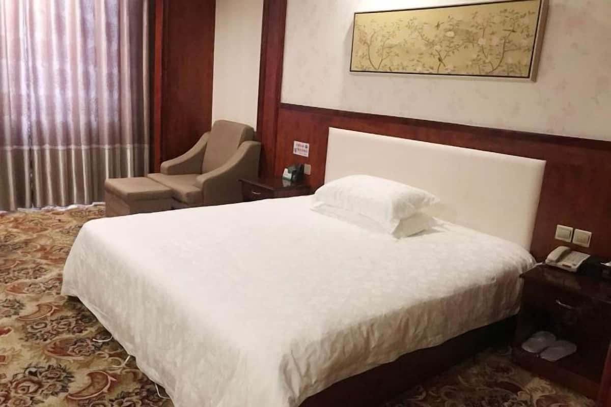 A hotel room with a large bed, a chair, a nightstand, and a wall-mounted telephone.