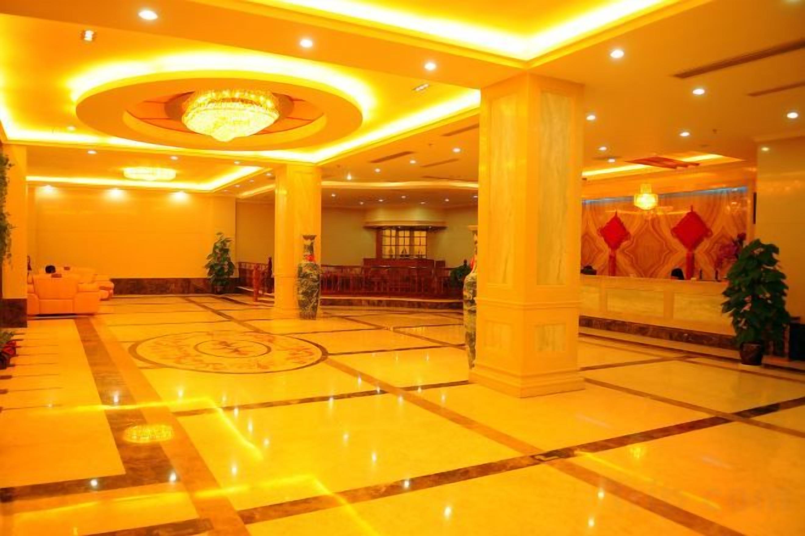 A hotel lobby with a marble floor, a reception desk, and a chandelier.