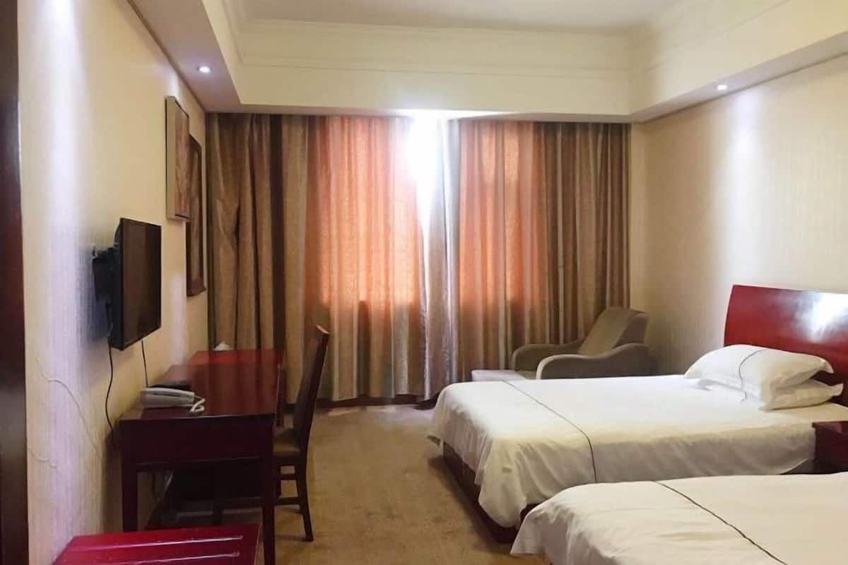 A hotel room with two beds, a desk, a chair, a TV, and curtains.