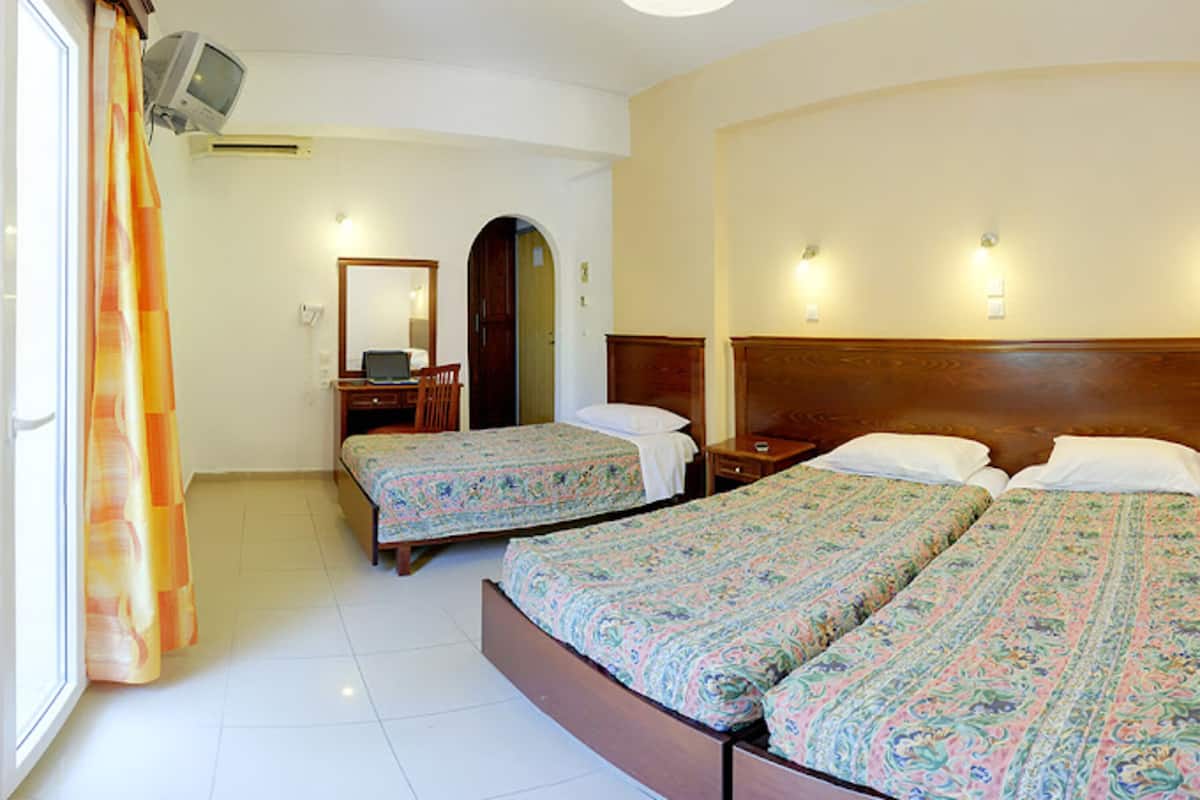 A hotel room with two single beds, a desk with a chair, a television mounted on the wall, and a window with curtains.
