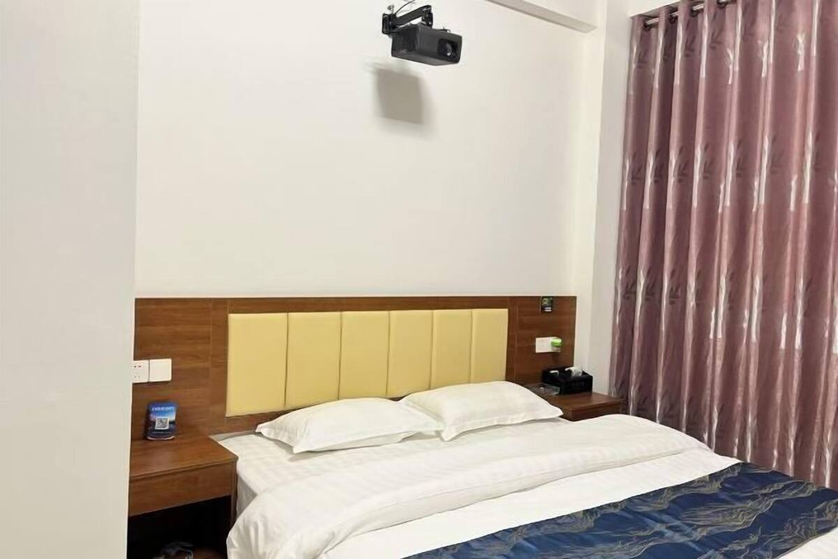 Ein Hotelzimmer mit Bett, Nachttisch, Wandprojektor und Vorhang.