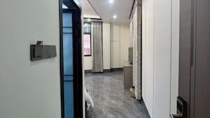 Un corridoio d'hotel con una porta, una piccola scrivania, uno specchio e una finestra con tende.
