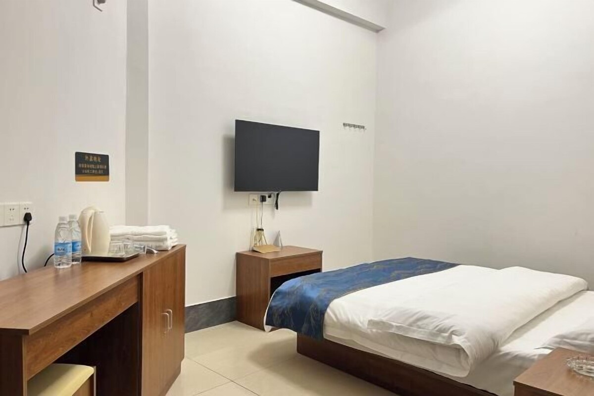 A hotel room with a bed, a desk, a television, and a small nightstand.