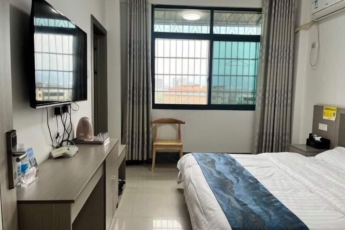 Ein Hotelzimmer mit Bett, Schreibtisch mit Flachbildfernseher, Stuhl und einem Fenster mit Vorhängen.