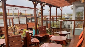 An outdoor patio area with wooden tables and benches, some with cushions. - Hoopers Sandy Beach Guest Rooms (Swansea)